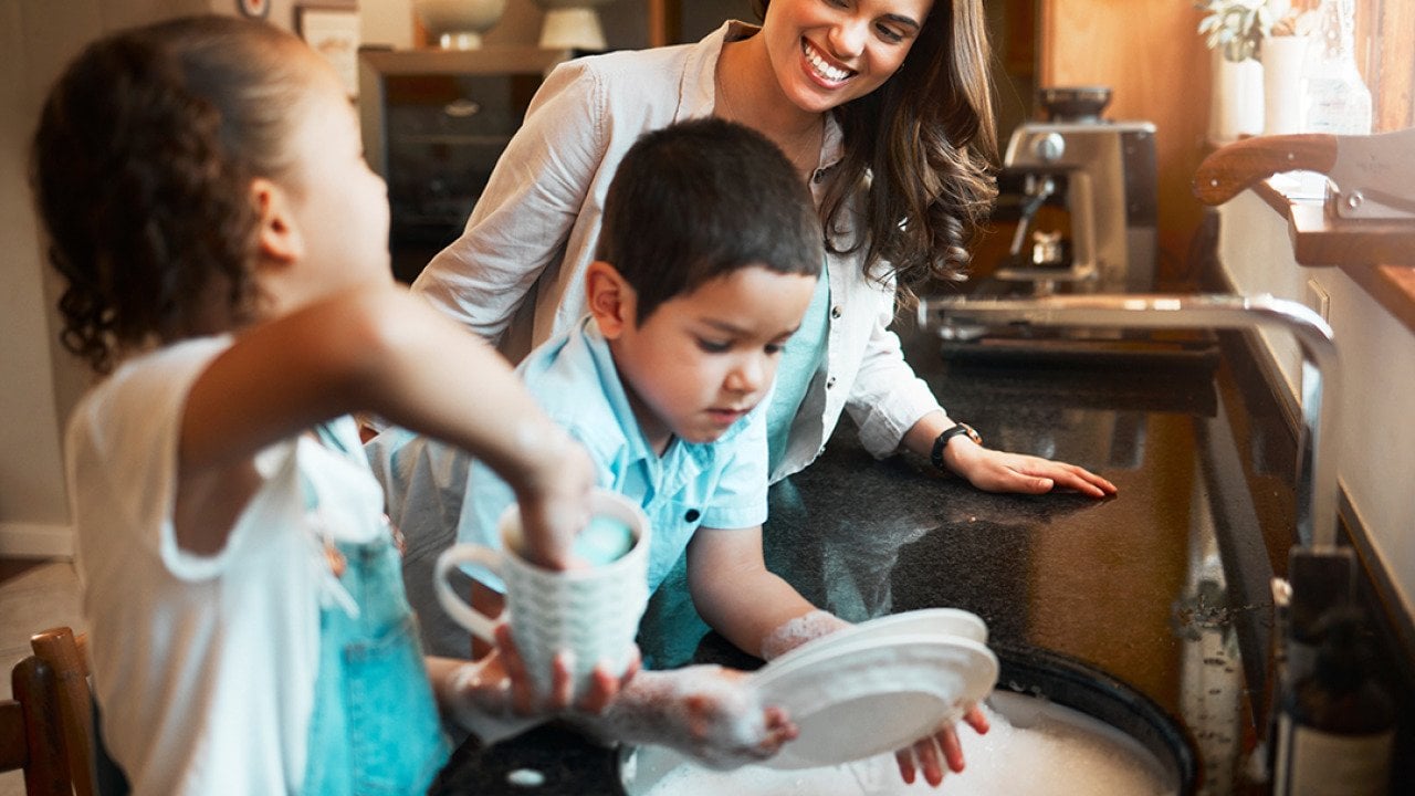 A mother with her two children washing dishes in the kitchen.
