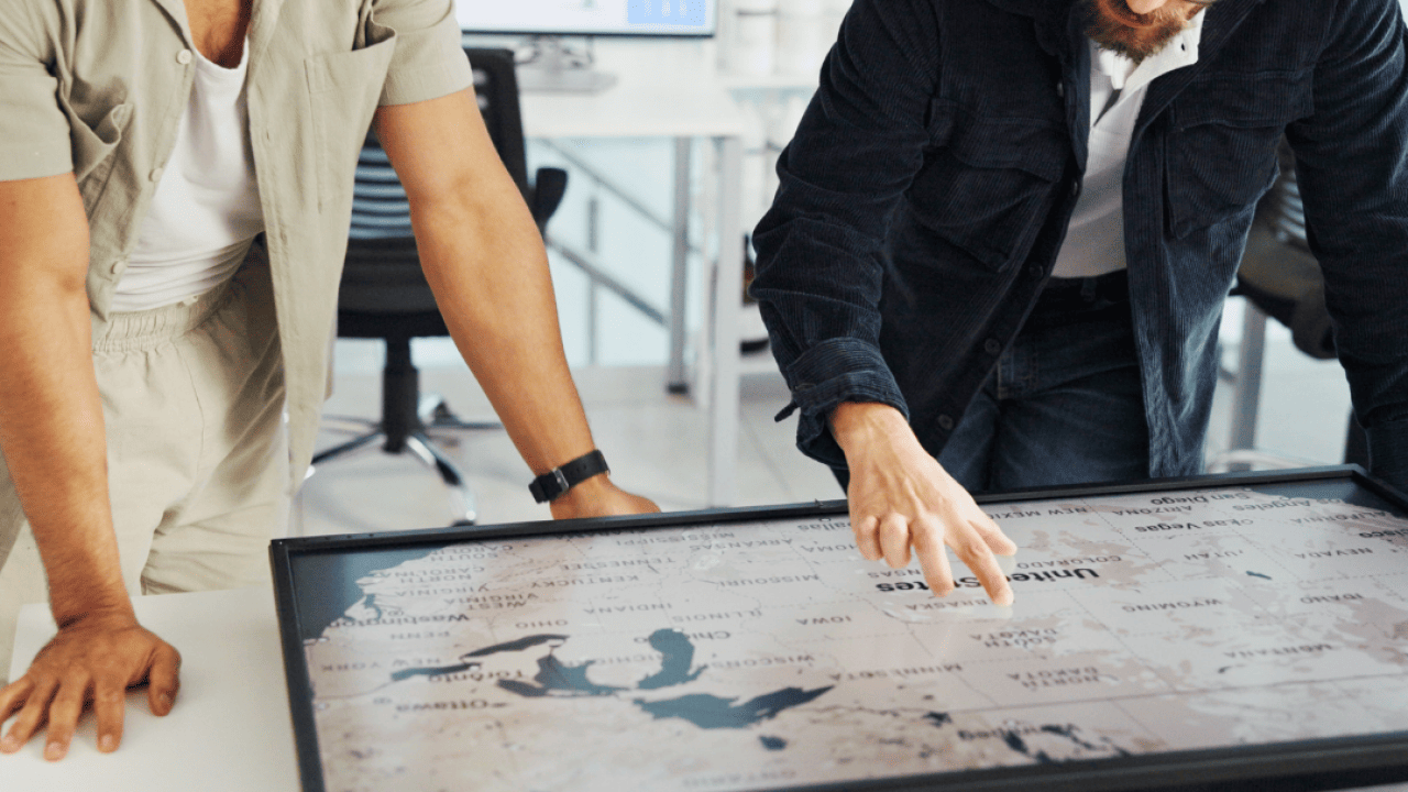 Two people looking at a U.S. map on a screen that is flat on a table in front of them.