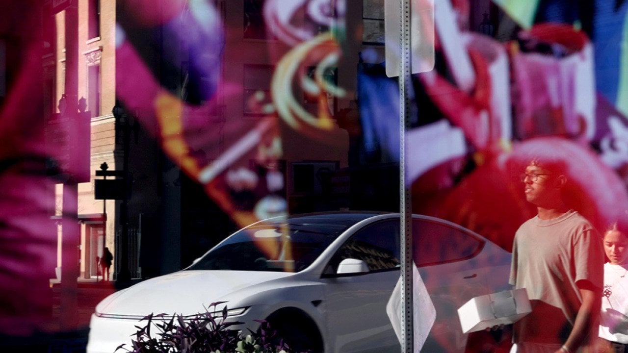 A Tesla car and pedestrians caught in a reflection on a storefront window.