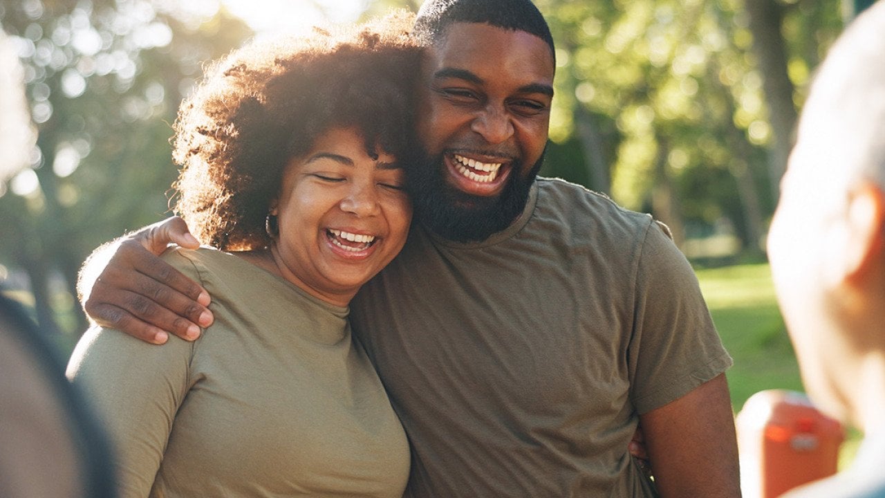 A happy Black couple hug and laugh outdoors.
