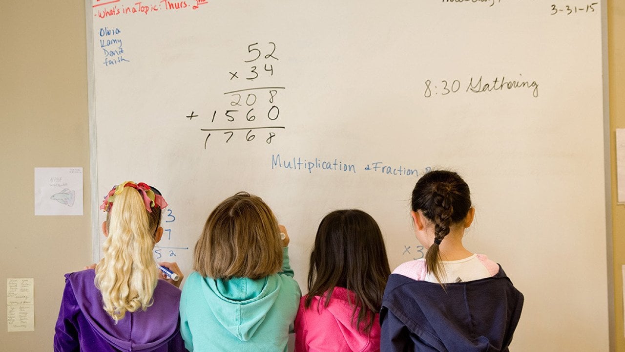 A group of children working to solve math problems on a whiteboard.
