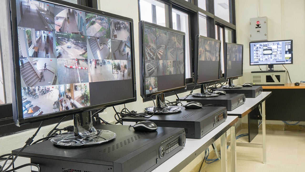 A security room with a row of monitors displaying multiple CCTV footage areas.