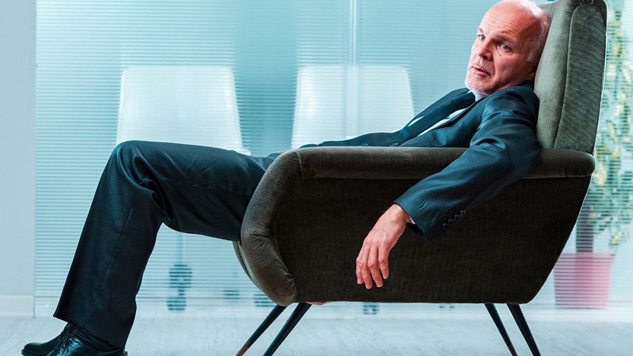 An elderly business person slouching in a chair at an office.