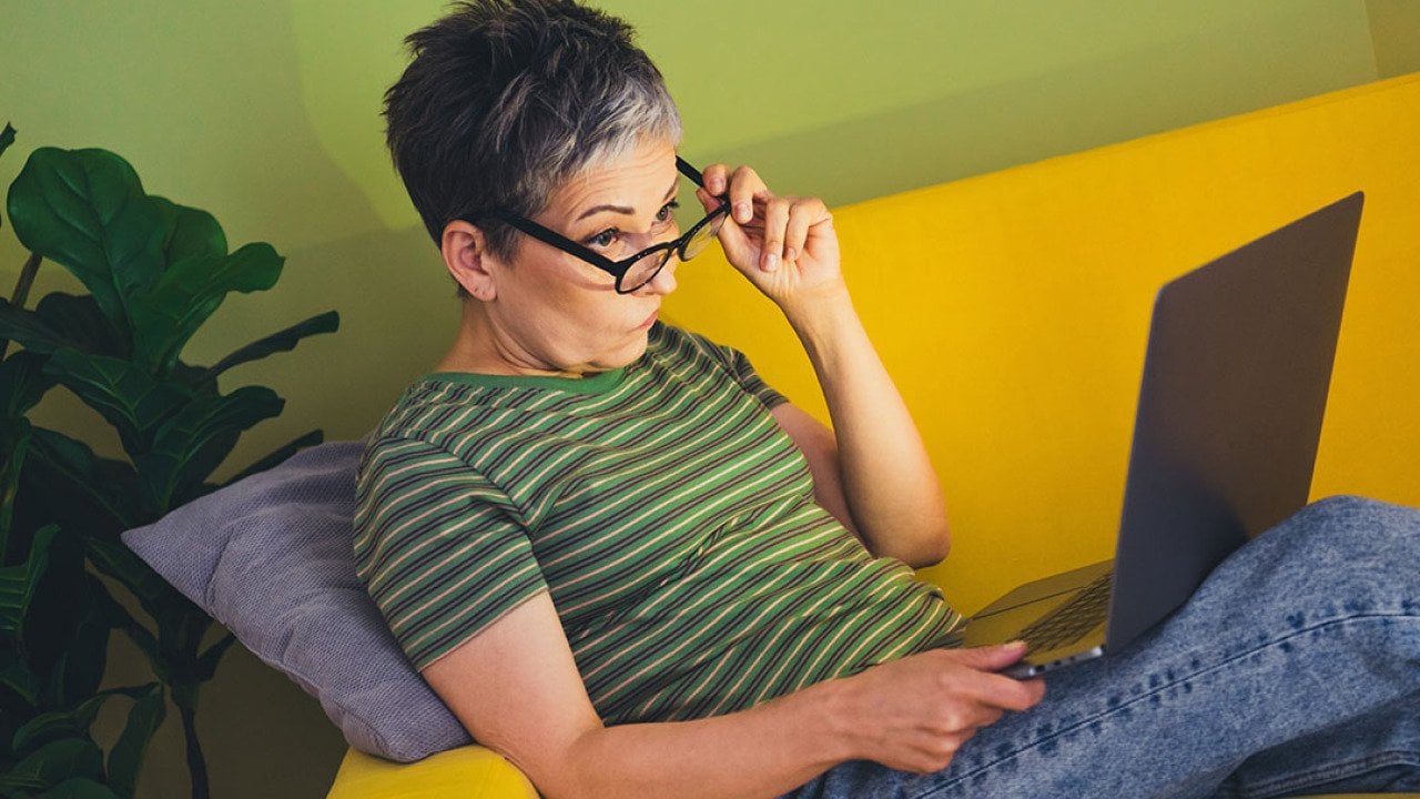 A middle aged woman skeptically browsing the internet at home.