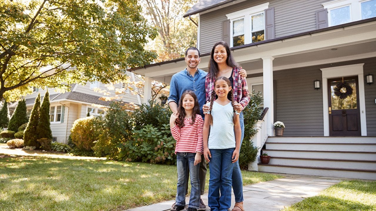 A family of four happily standing in front of their home for a photo.