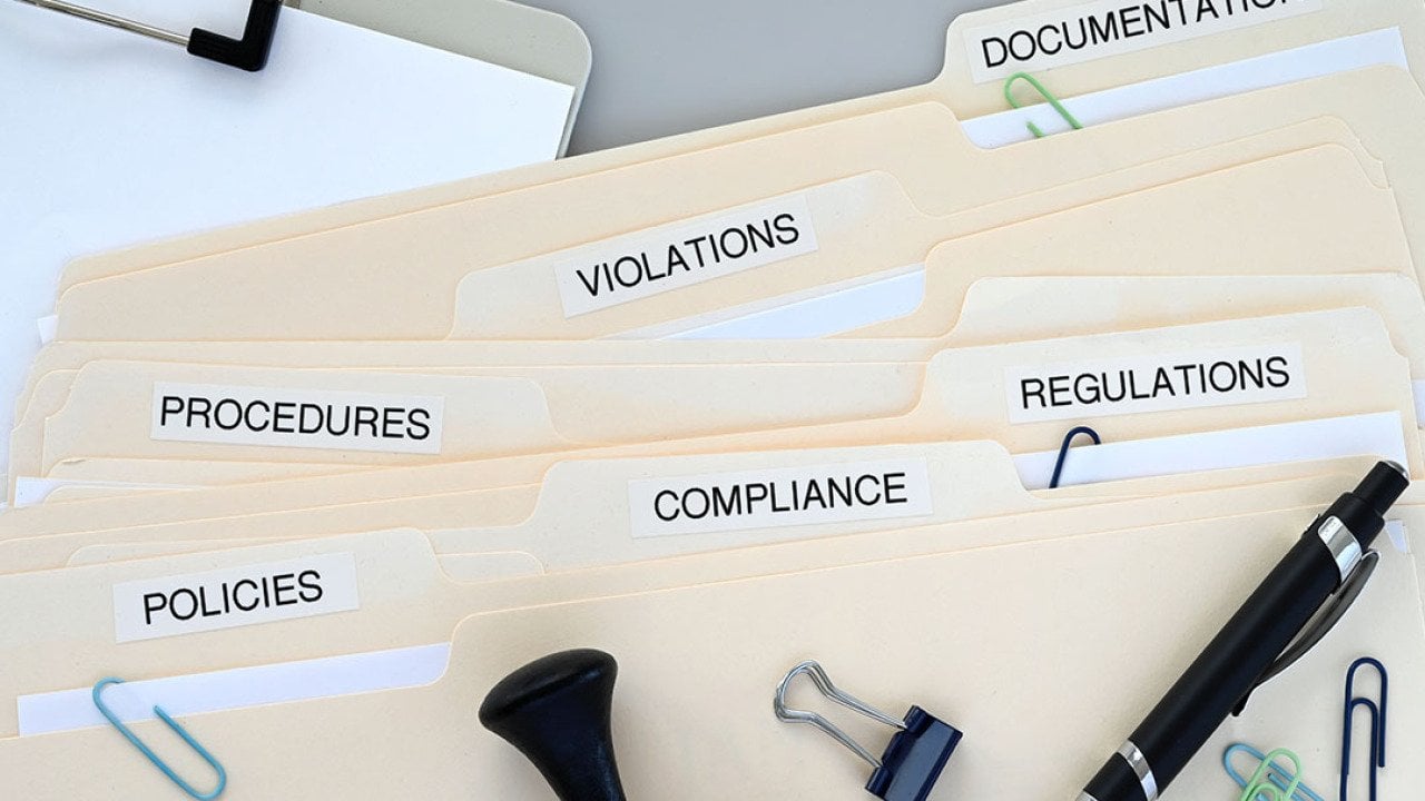 Folders of compliance and policy documents on a desk.
