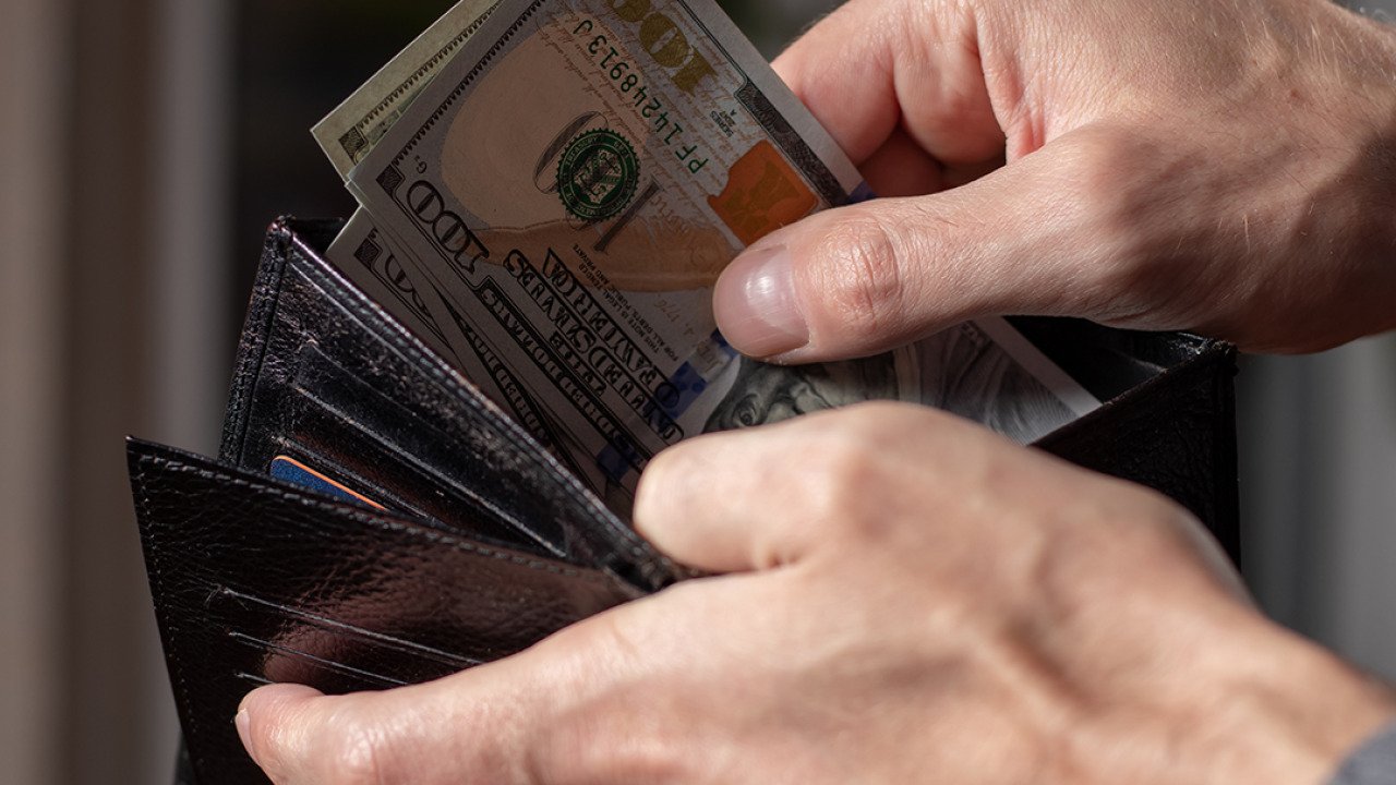 A person taking out dollar bills from a wallet.