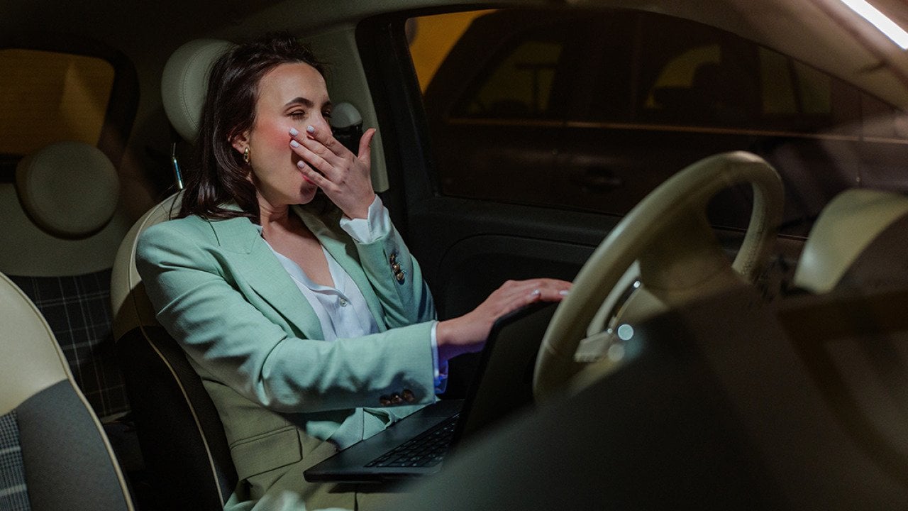 An employee yawning inside her car after work. 