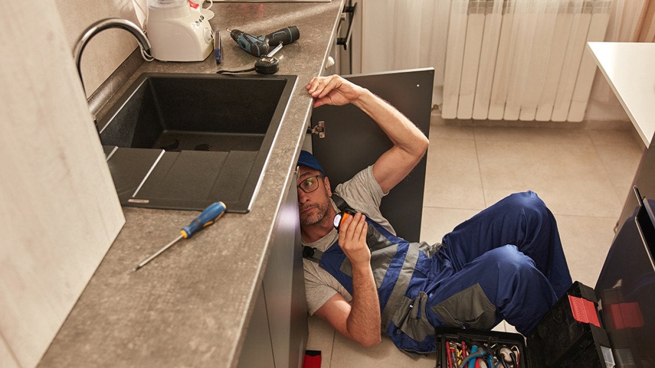 A plumber fixing a water pipe under the kitchen sink.