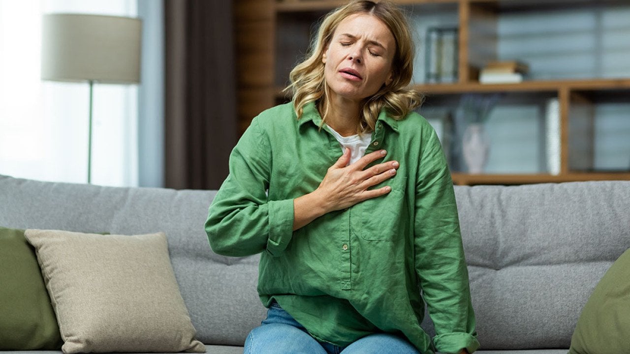 A woman sitting on a sofa holding her chest due to pain.