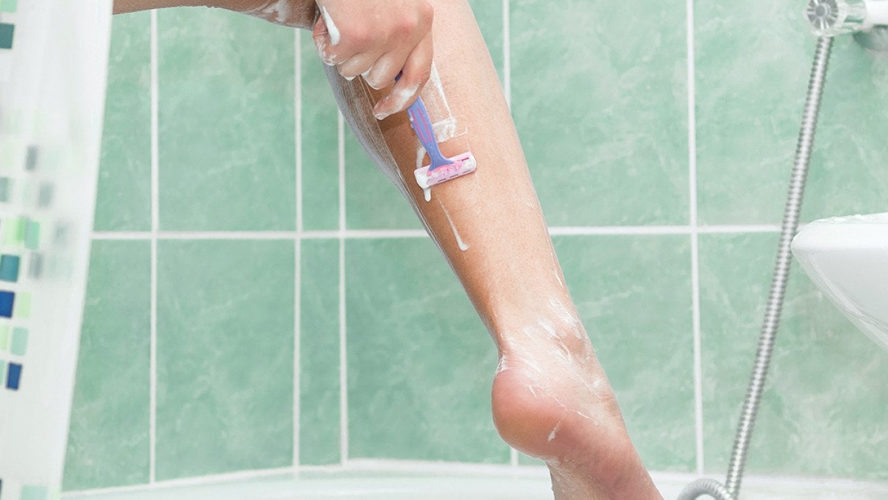 A close-up of a person shaving her leg in a bathroom. 