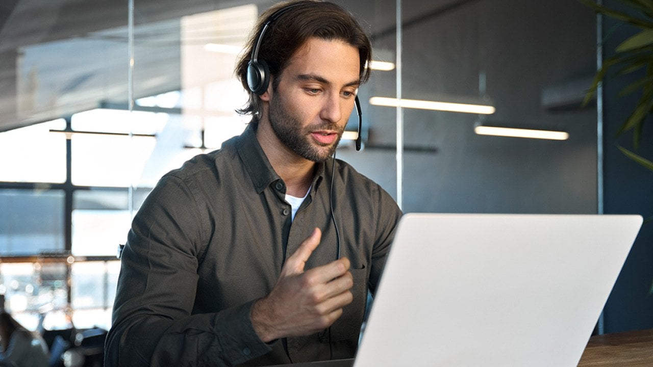 A male customer support service employee in an office working on a call with a client.