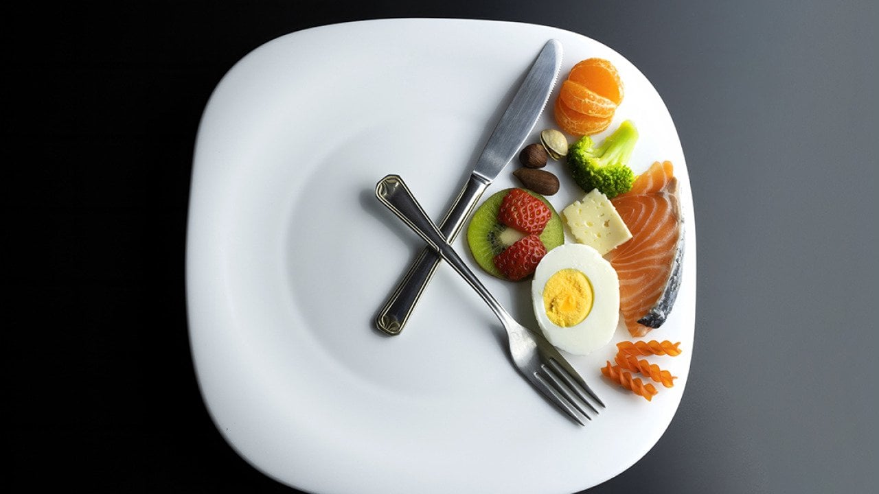 A plate of healthy ingredients simulating a clock with its hands represented by a knife and a fork as a concept of intermittent fasting.
