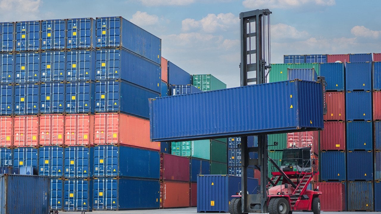 A forklift lifting a container van in a shipping yard.