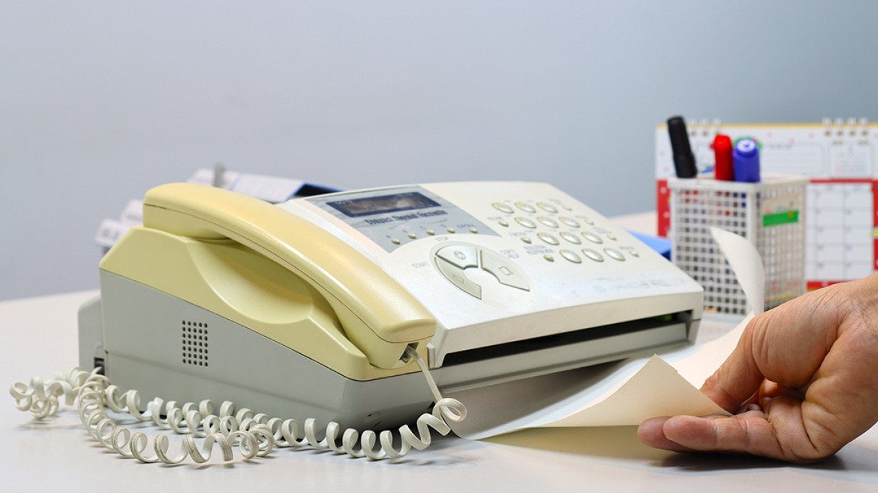 Person feeding a yellowing fax machine paper.