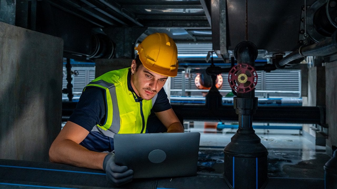 An industrial engineer viewing a laptop while checking an HVAC pipeline system.