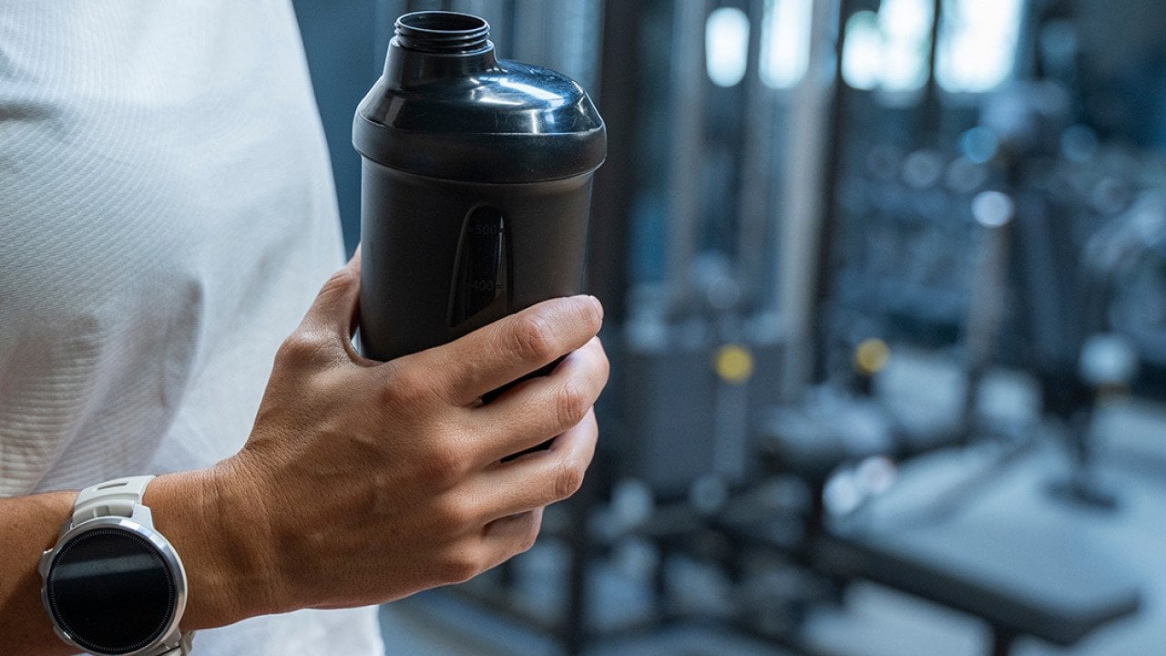 A person holding a water bottle during her workout in a gym.