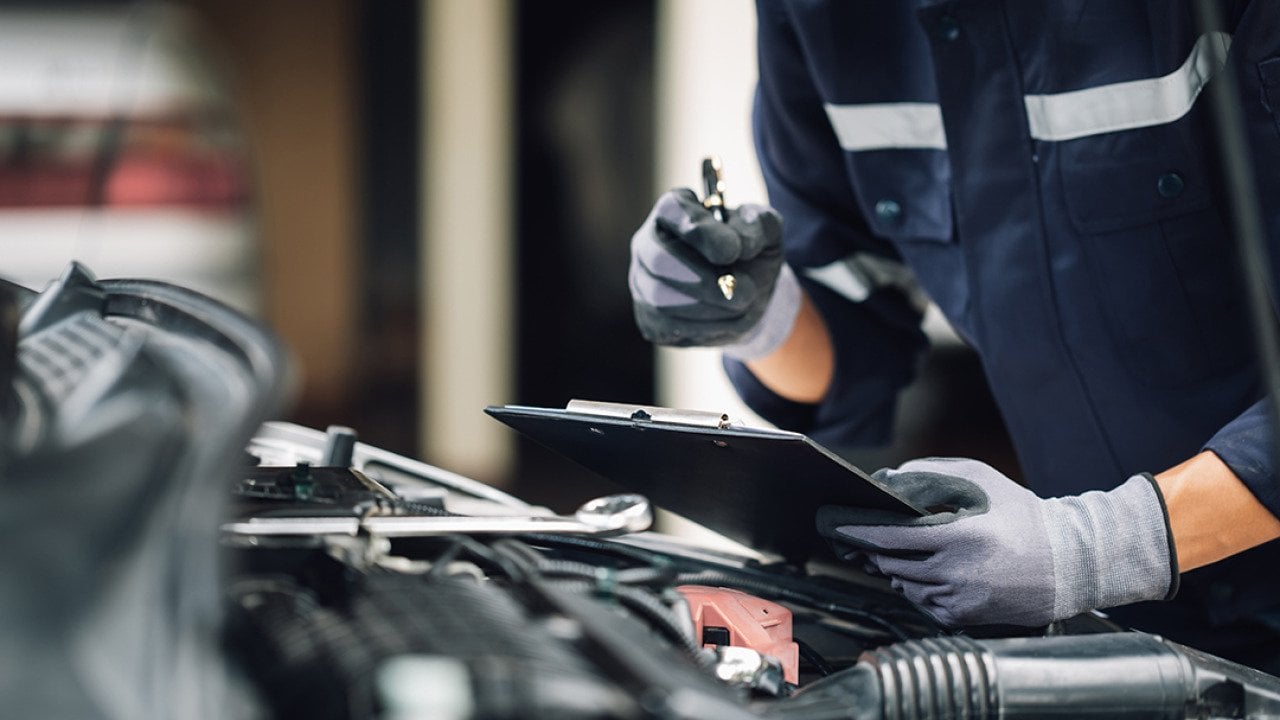 A car mechanic doing a checklist while looking at an engine.
