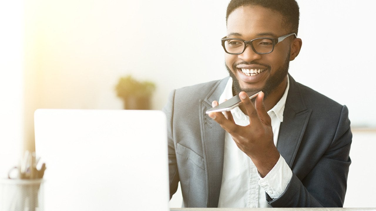 A happy young black businessman using voice assistant on his smartphone.