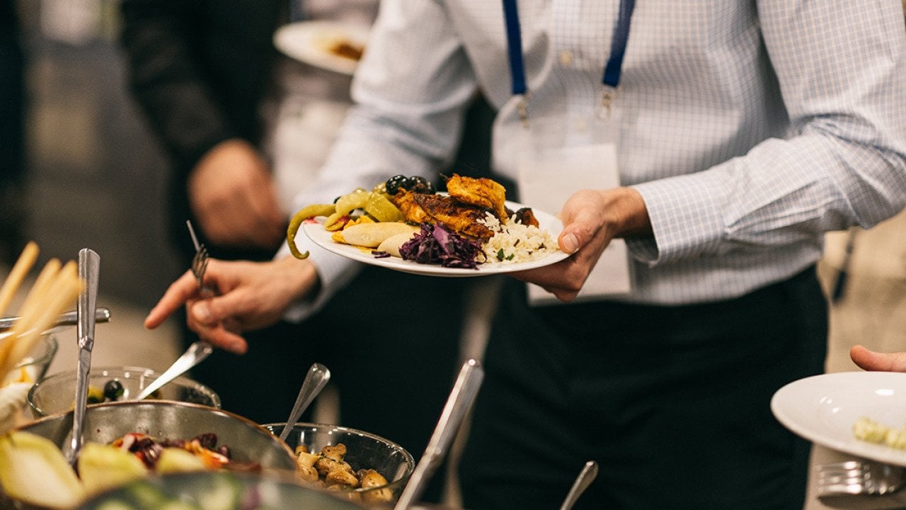 An employee holding up a plate of Mediterranean food from a catering event.
