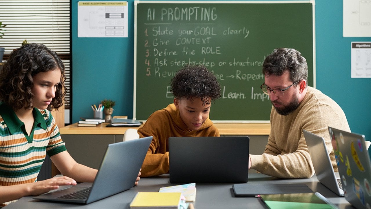 A male teacher guiding students in a classroom in using AI.