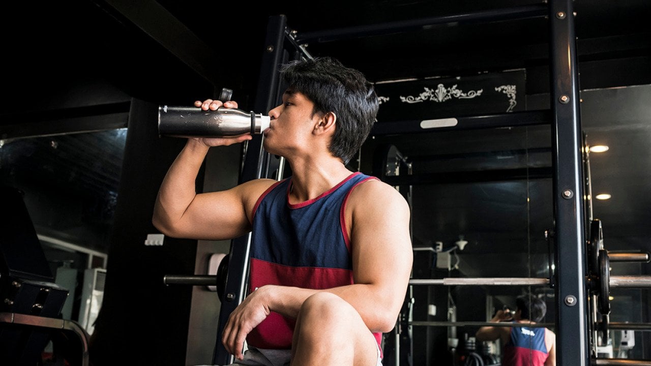 A young, fit man drinking water inside a gym.
