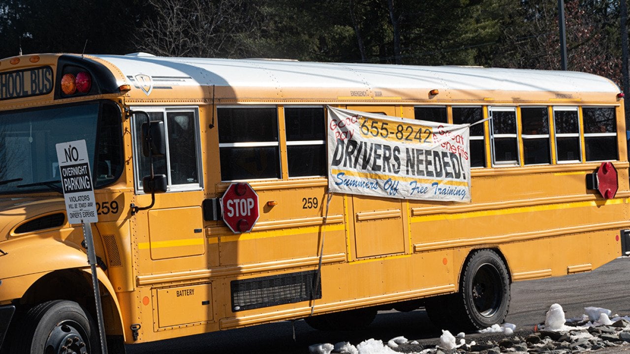A school bus with a hanging display of drivers needed during a driver shortage in Windsor, New York, USA.