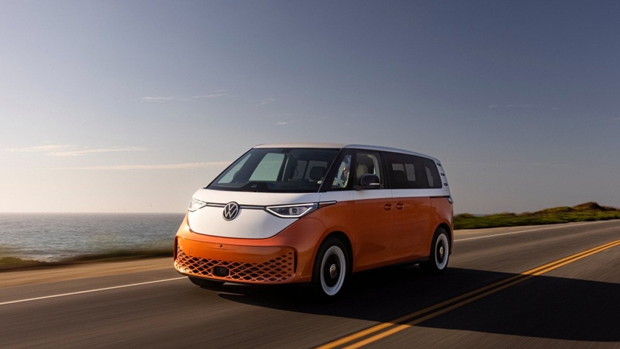 Candy White over Energetic Orange 2025 Volkswagen ID Buzz driving on road next to ocean.