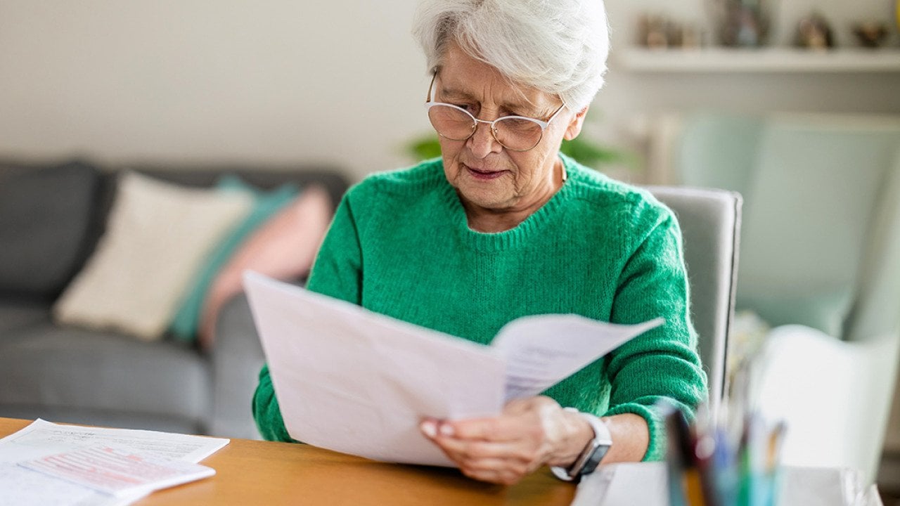 A senior woman sitting in the living room and doing paperwork.