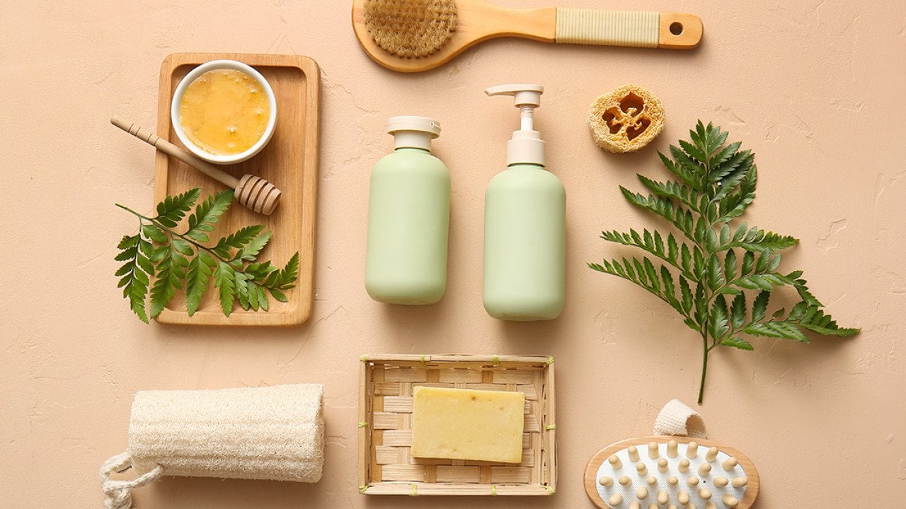Soap, body scrub, brushes and bathroom essentials laid on a beige surface.