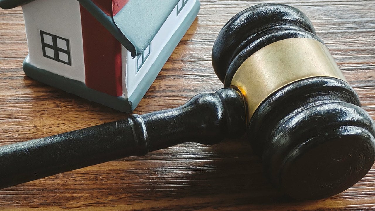 A miniature house and a gavel in a wooden surface.