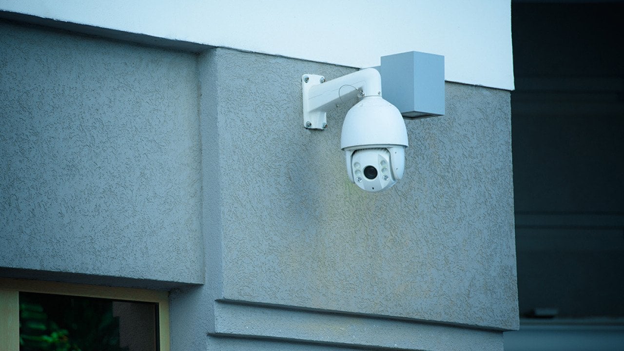 A view of a security camera on the facade of a gray building.