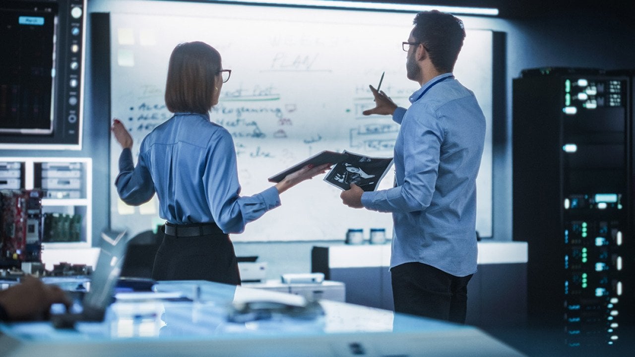 A team of two professional engineers using a digital tablet to discuss a manufacturing plan.