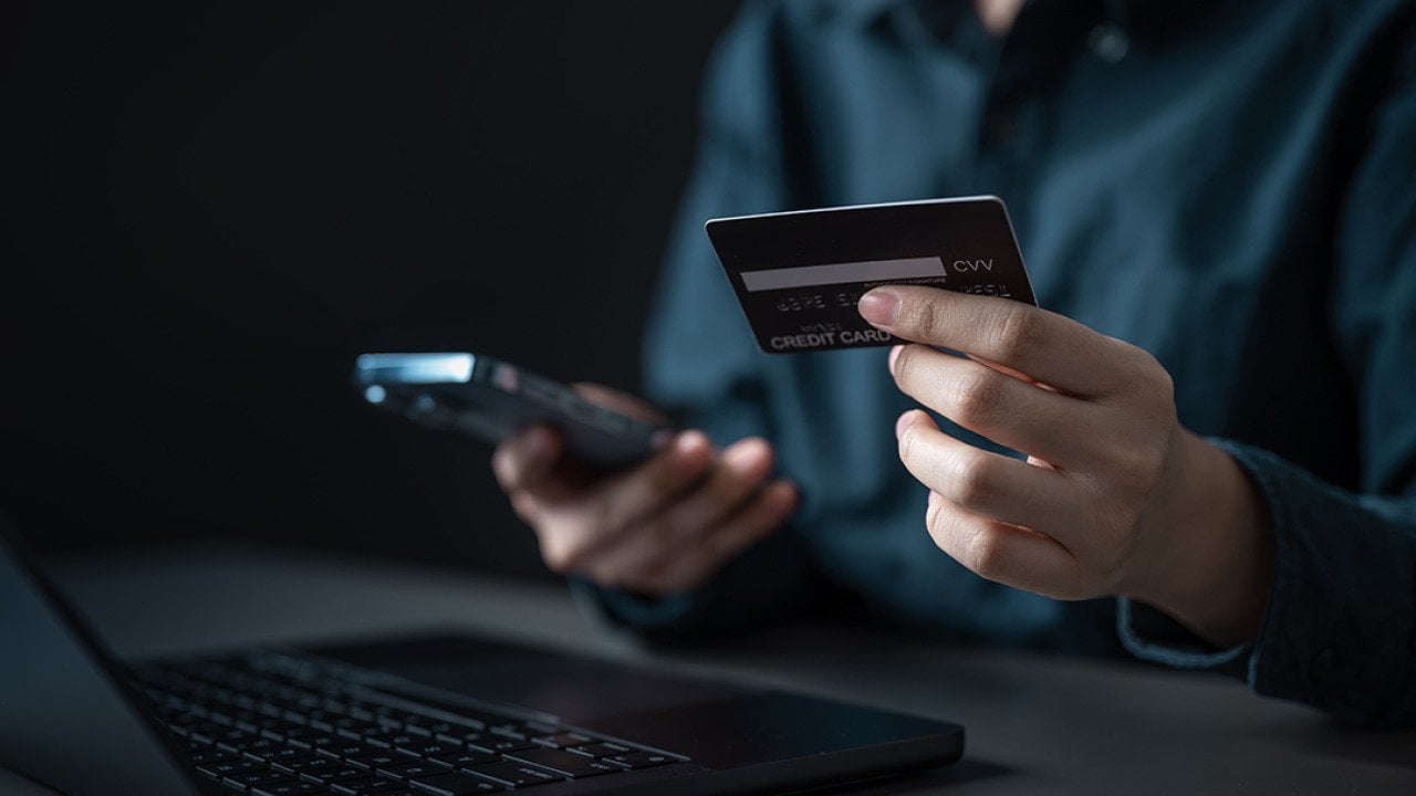 A person checking credit card details from a smartphone and laptop.