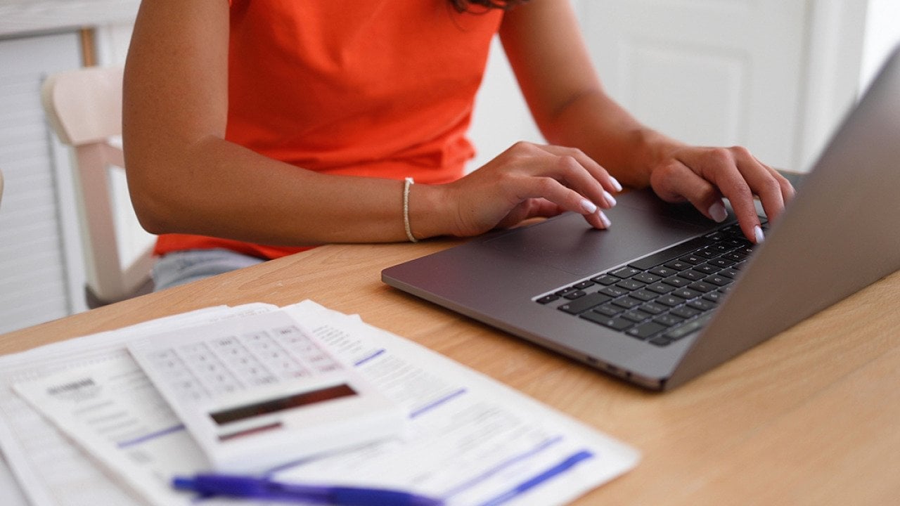A woman organizing finances at home using a laptop and calculator over documents.
