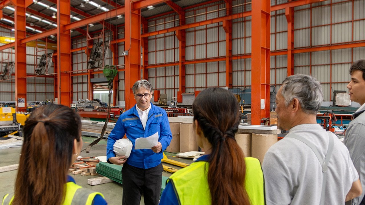 A supervisor leads his team for a briefing inside a manufacturing factory.