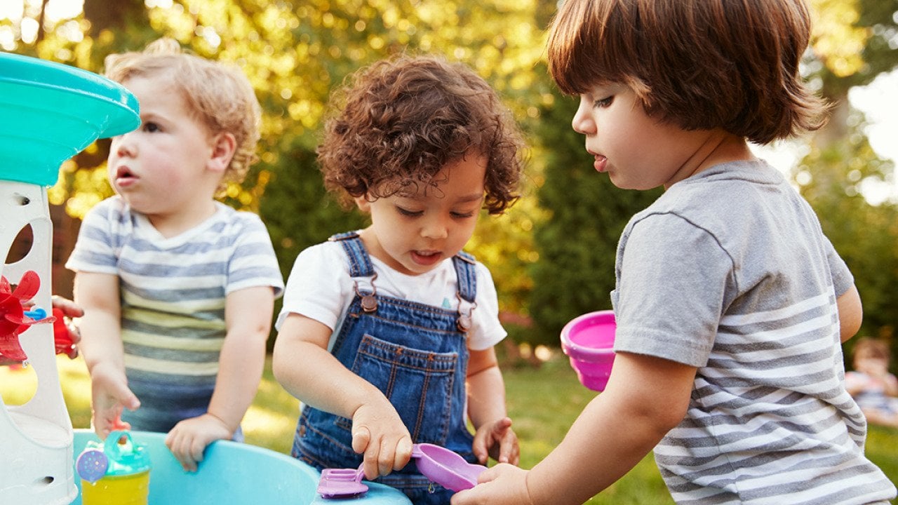 Three little children playing around a water table in a garden.