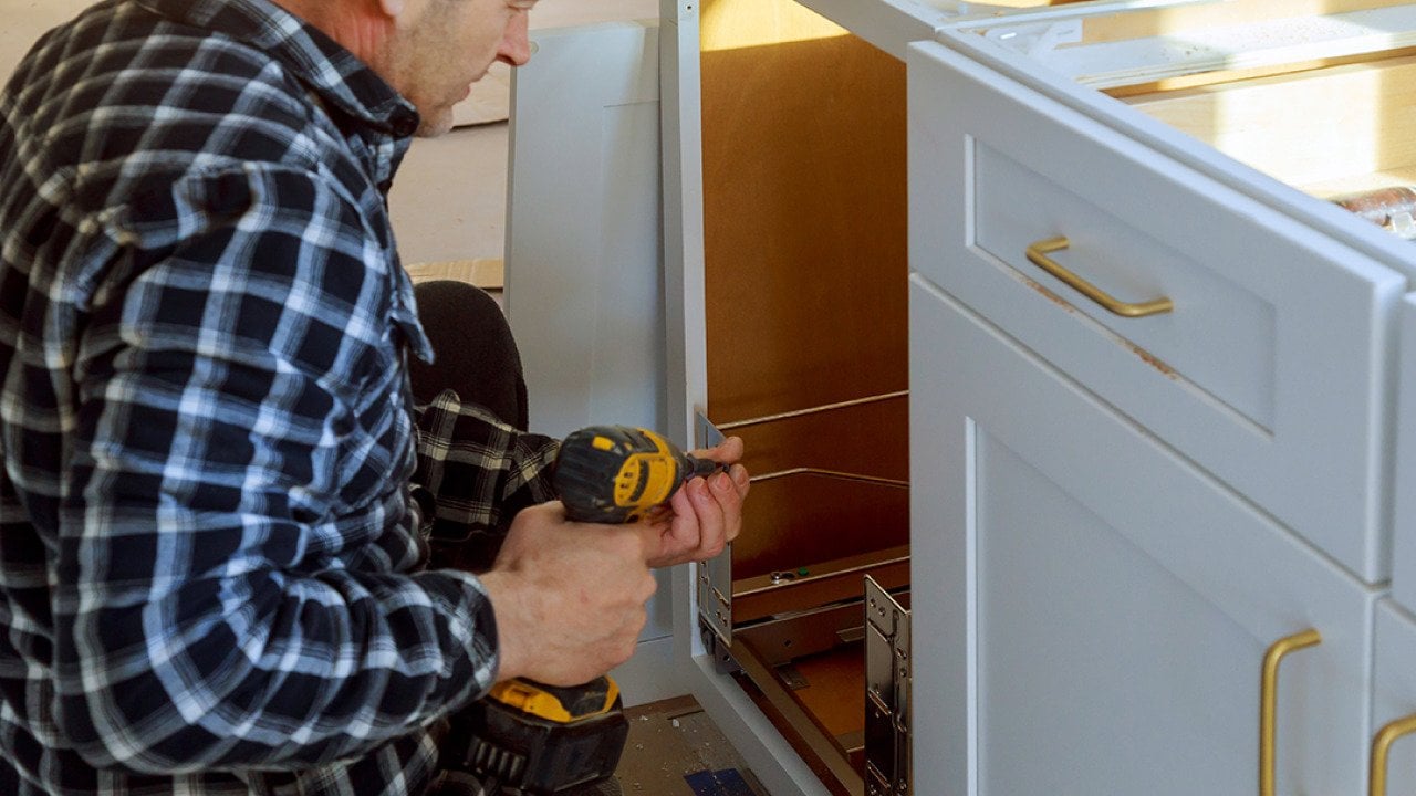 A woodworker installing a drawer for a garbage bin in a kitchen.