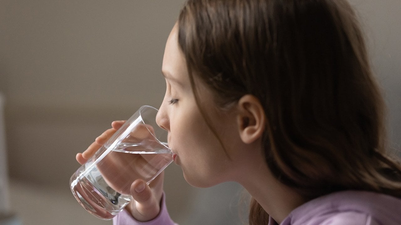A young dehydrated teenage girl drinking a glass of water.