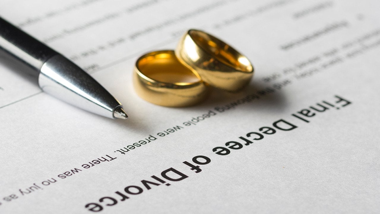 Marriage rings and a pen on top of a divorce decree form. 