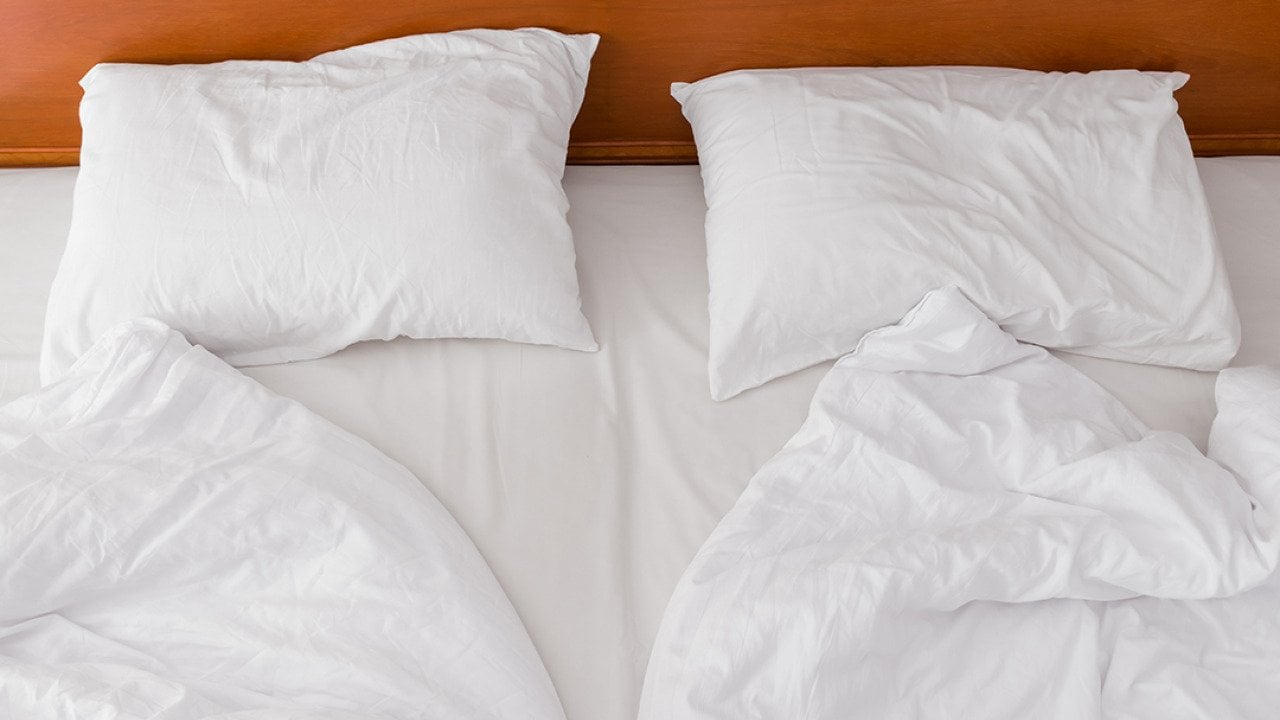 A view from above of an unmade bed with two duvets and white pillows.