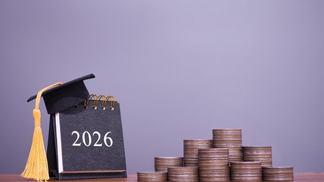 A 2026 calendar with a graduation hat and stacks of coins in a desk.