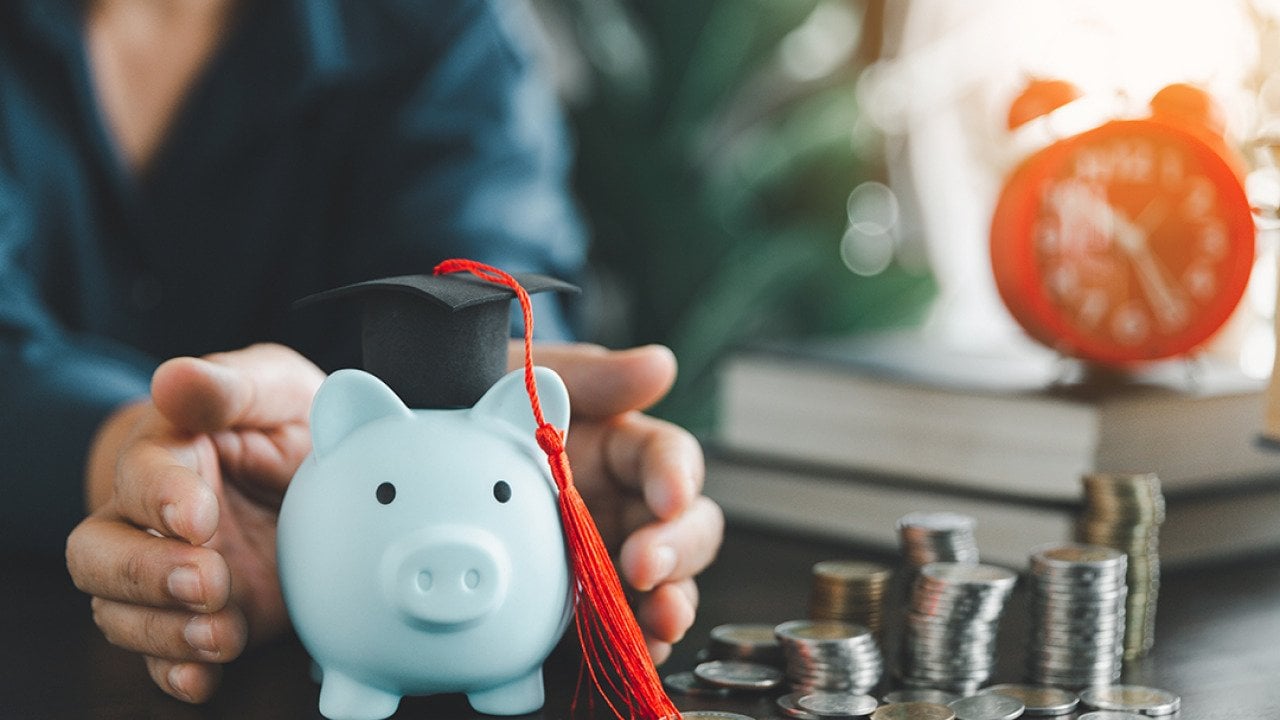 Person protecting a piggy bank with a graduation cap as a concept of saving money for education.