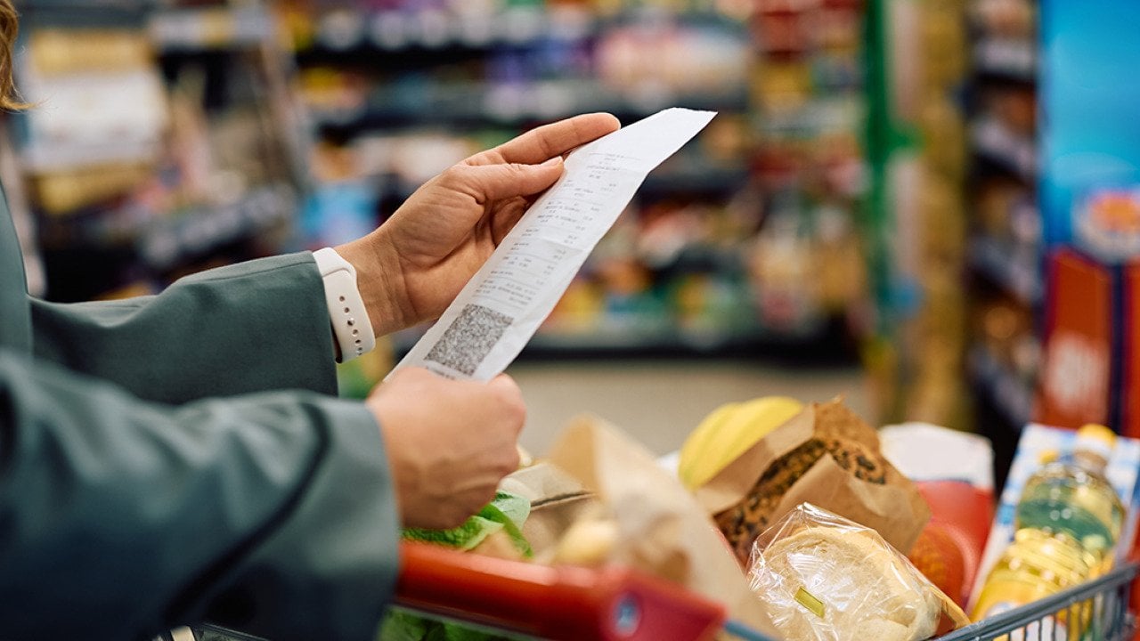 Person looking at a long grocery shopping bill while still at a supermarket.