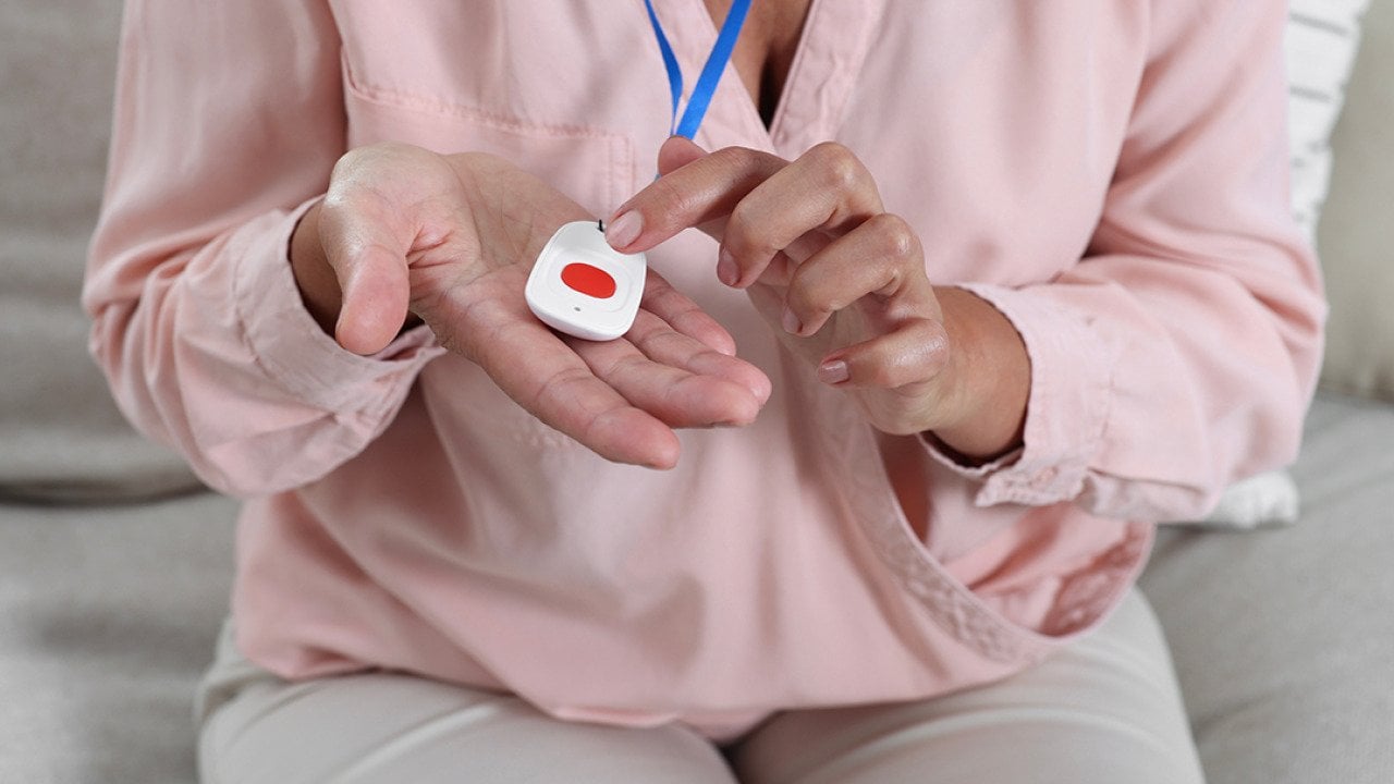 Woman pressing the button of a pendant medical alert system device at home.