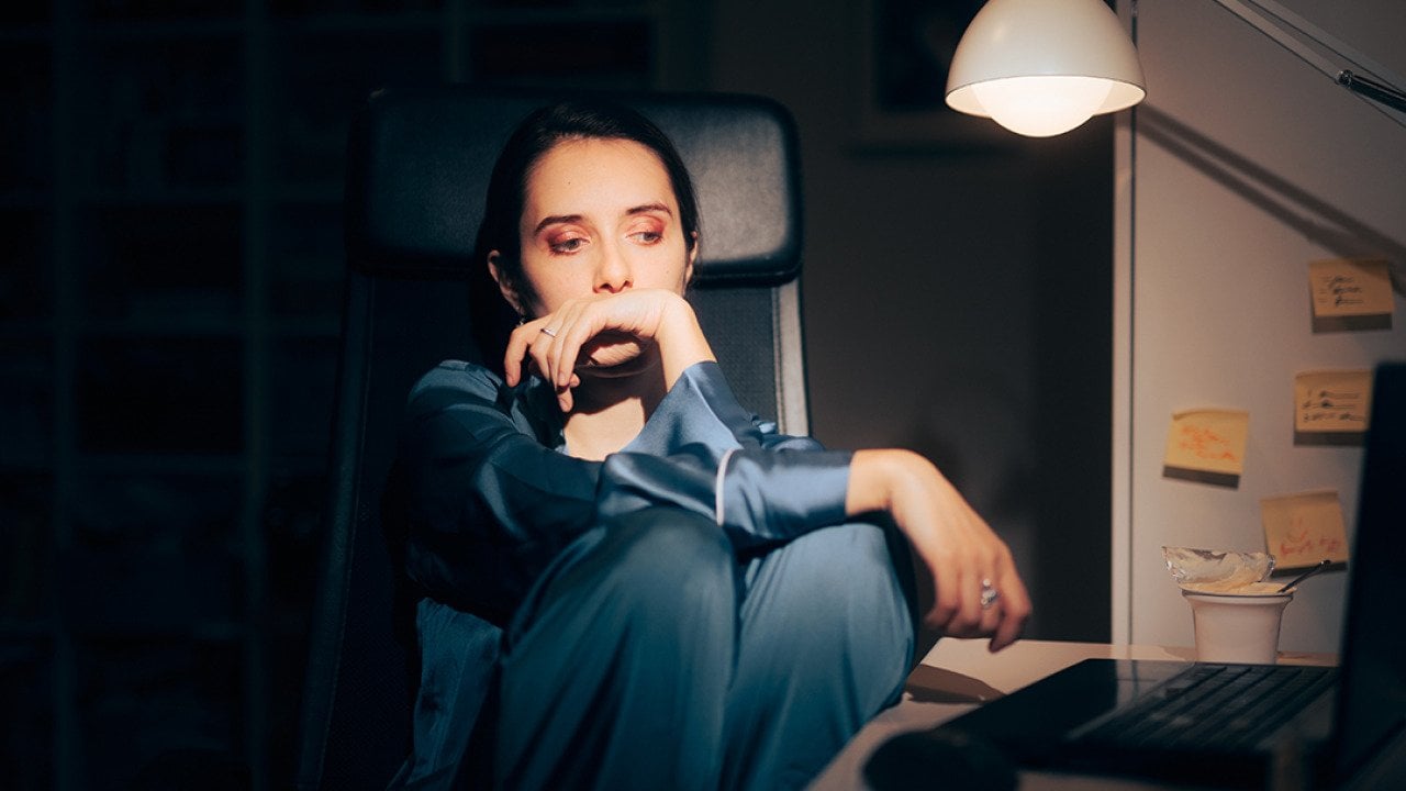 A young woman working at night looking worried staring at her laptop.