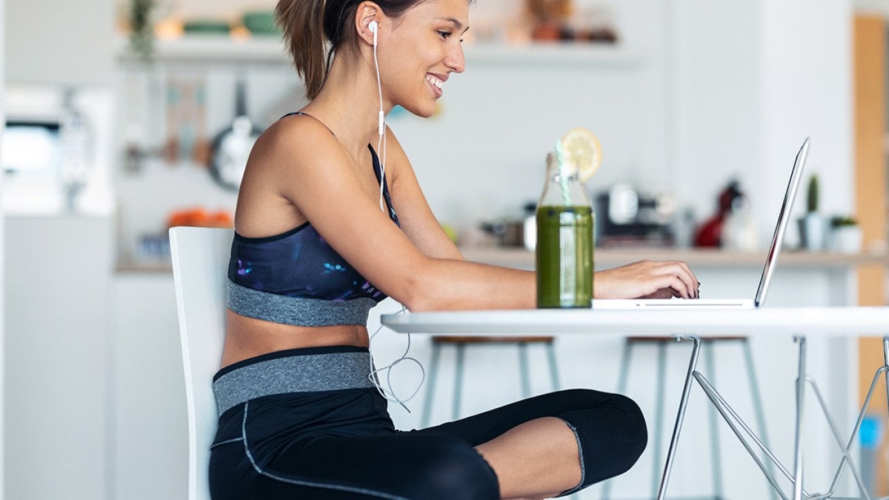 A young woman in athleisure wear working from her home's kitchen.