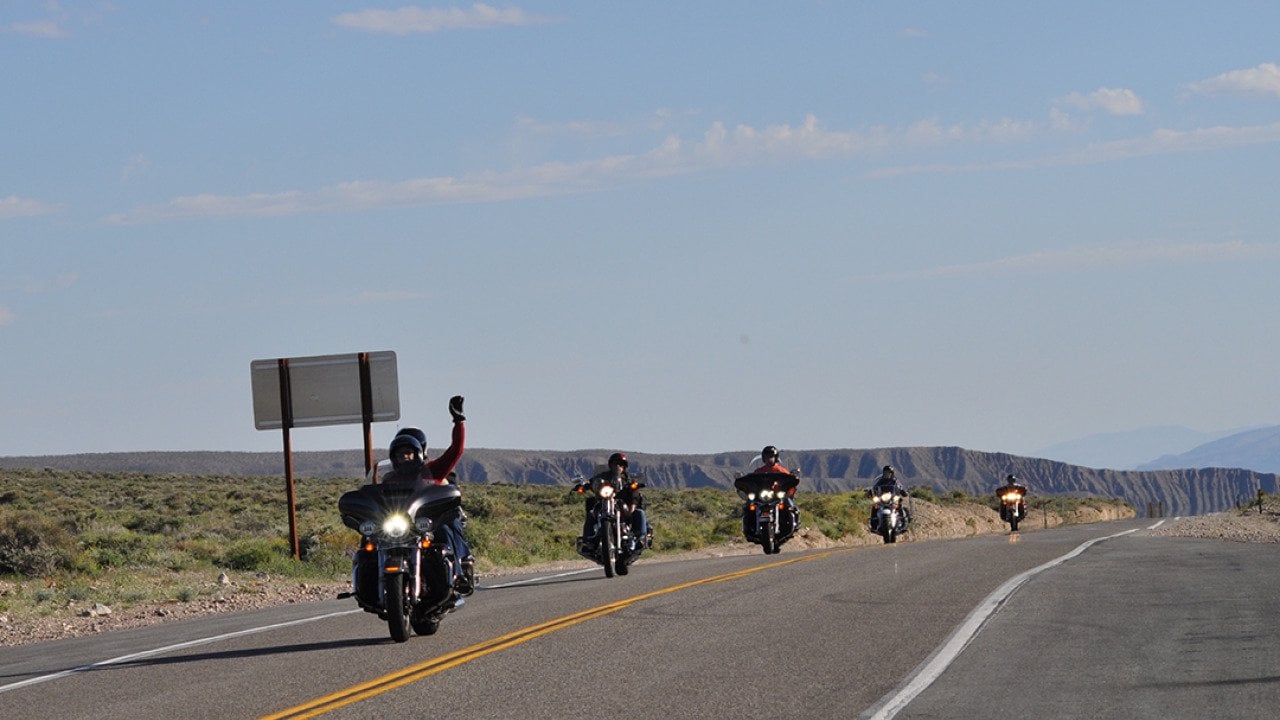 Motorbike riders raising hands for a photo opportunity while passing a road in California, USA.