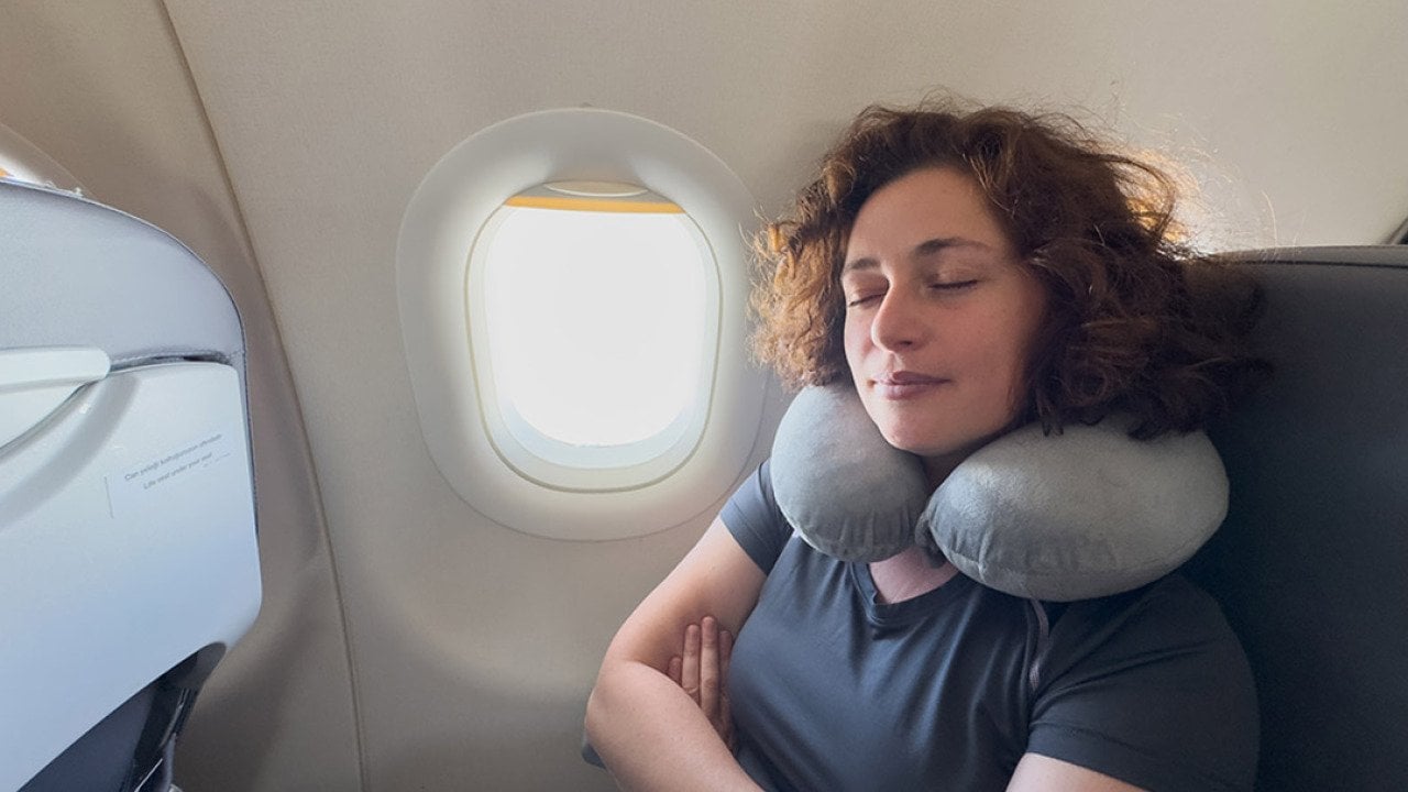 A person sleeping with a neck pillow from her seat in a plane.