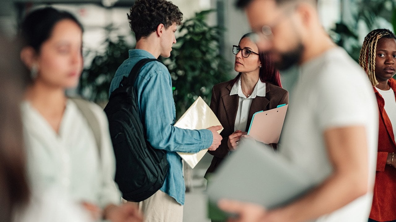 A college student talks to a professor in a campus hallway.
